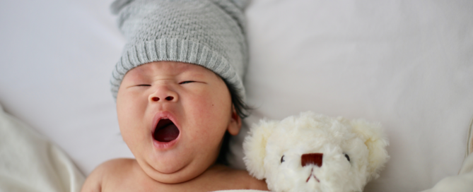 Niño con un gorro de orejas, bostezando y durmiendo al lado de un oso de peluche